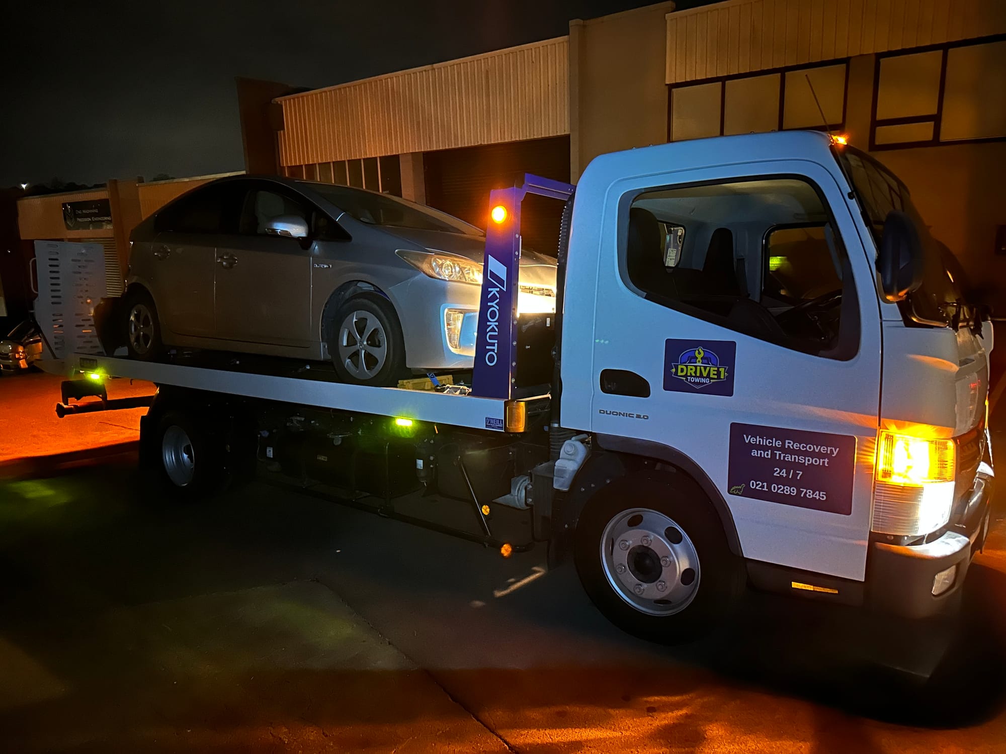 Silver Toyota Prius secured on the Drive1 Towing flatbed at night.