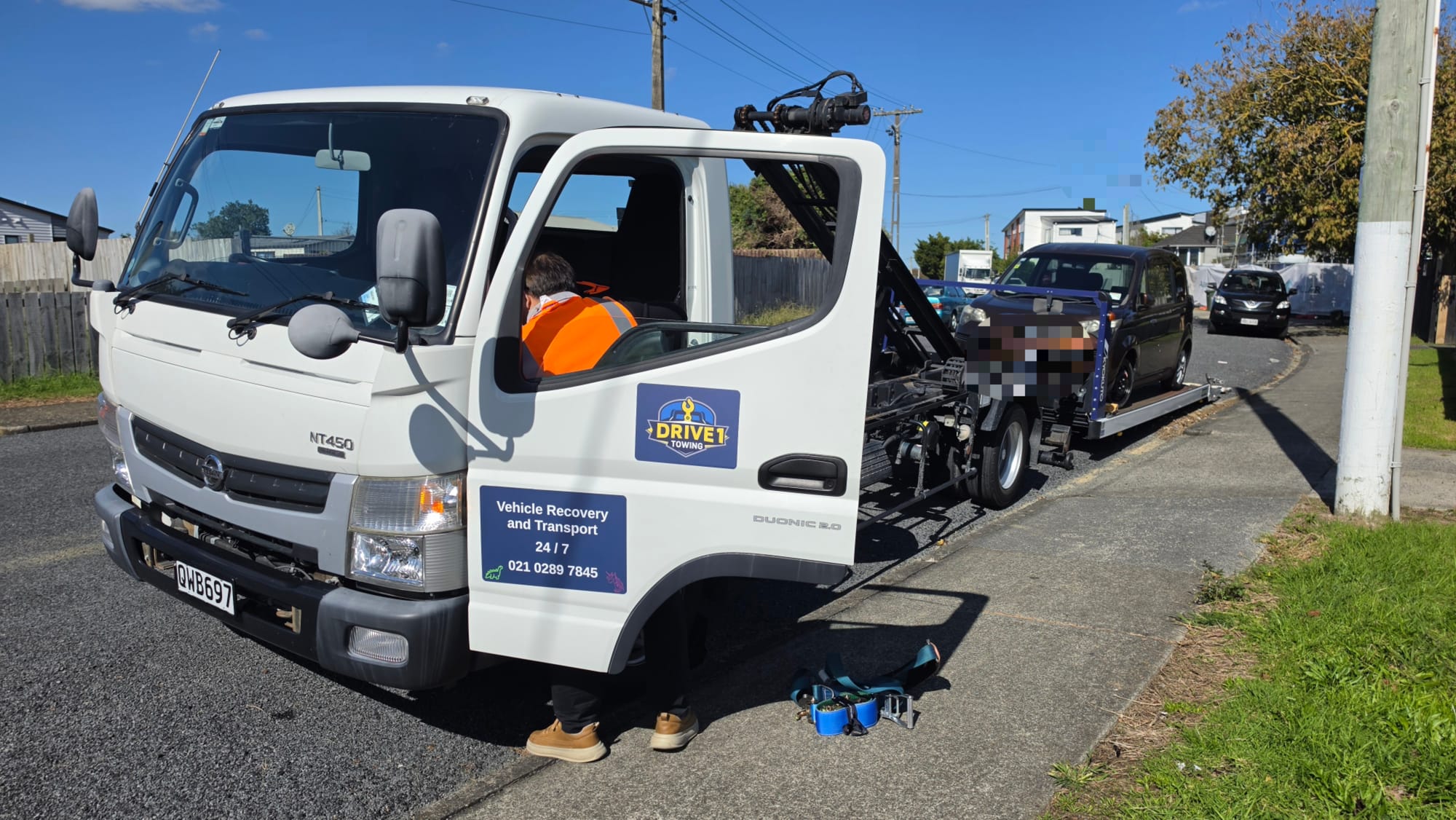 Drive1 Towing flatbed loaded with a white work van against an Auckland skyline.